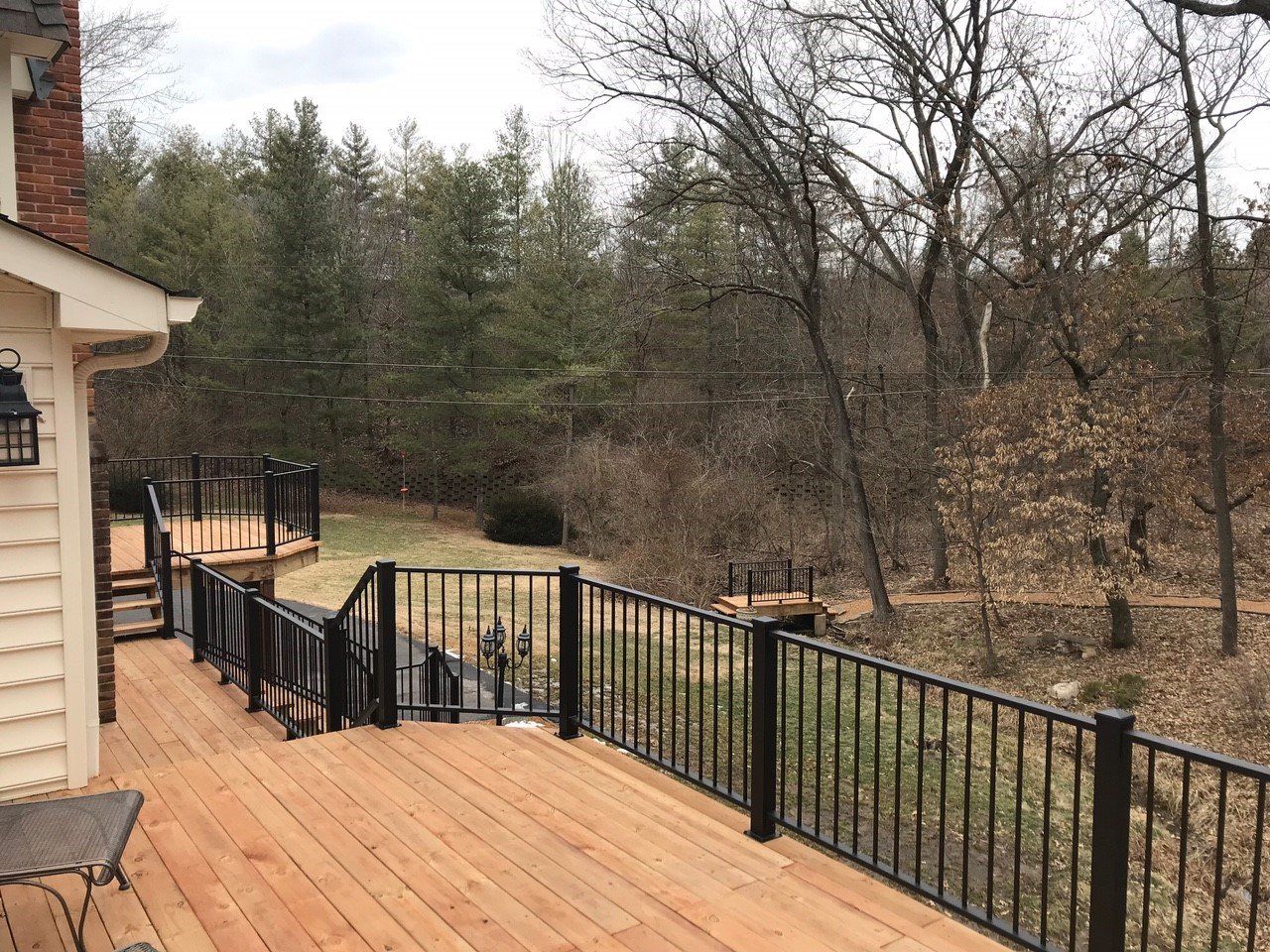 Wooden deck with black railing beside a house, overlooking a wooded yard in winter.