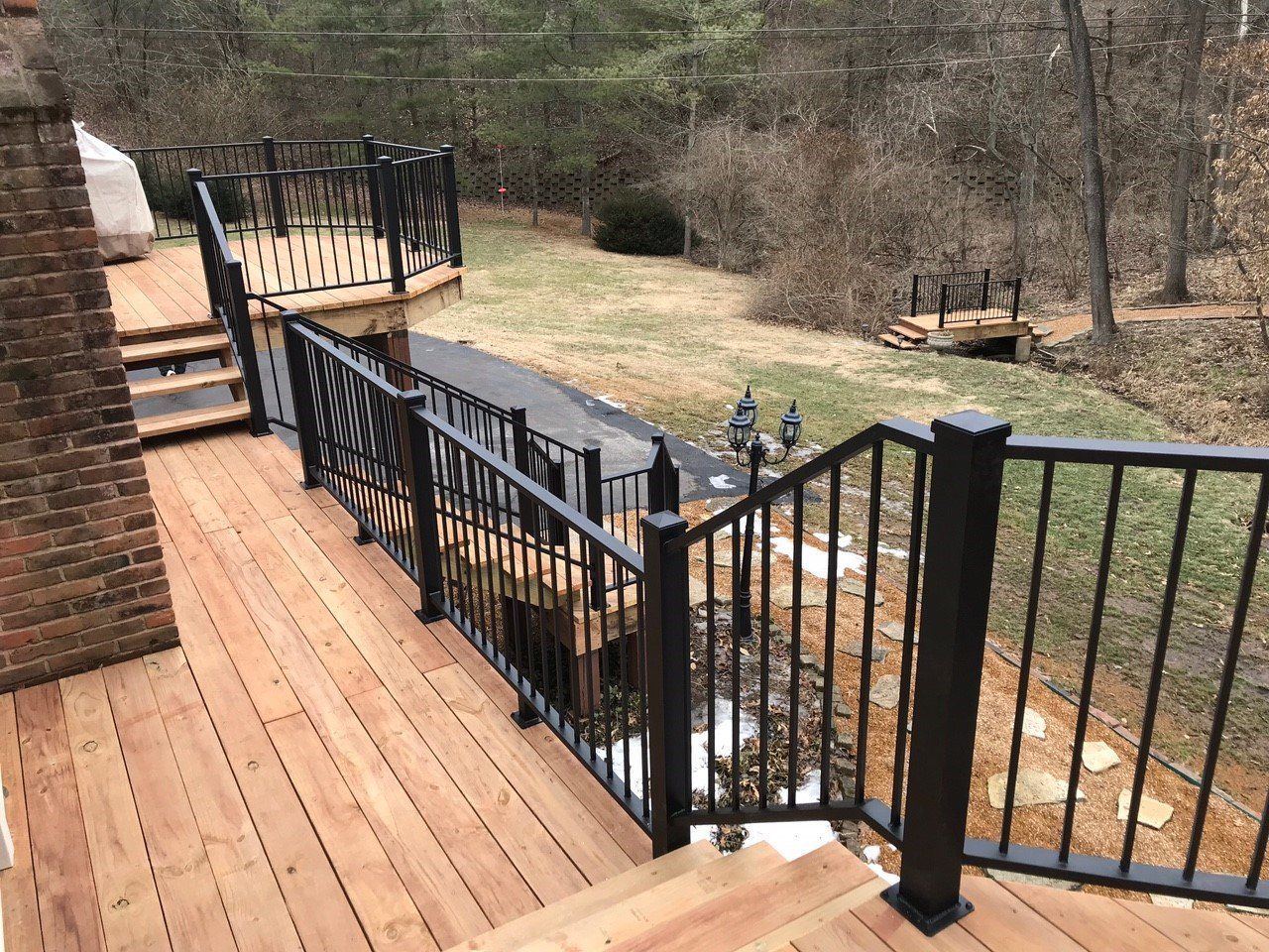 Wooden deck with black metal railings overlooking a yard and wooded area