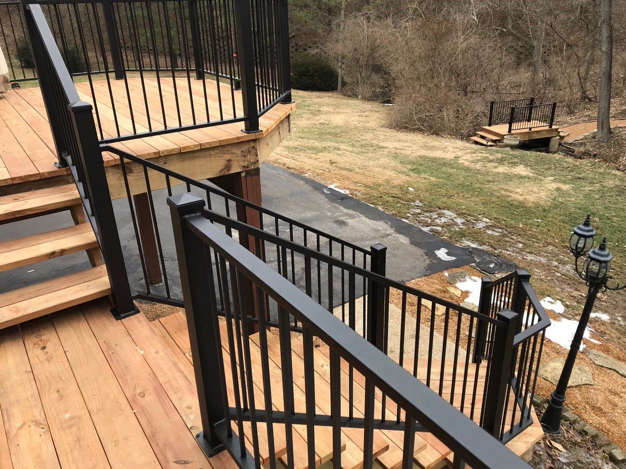 Wooden deck stairs with black railings beside a grassy backyard and trees