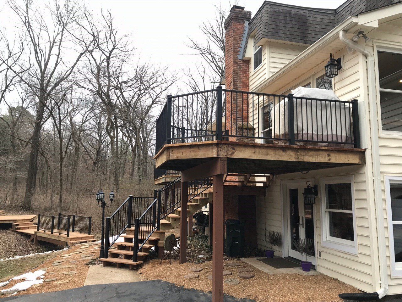 Raised deck with black railing attached to a white house beside a wooded backyard