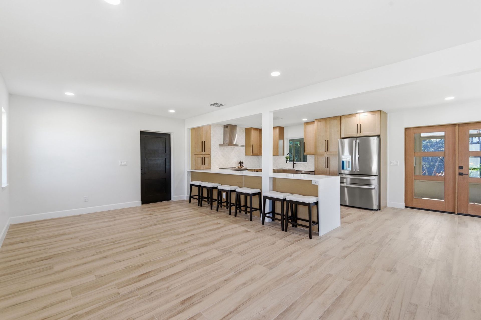 An open-concept kitchen with light wood floors, white walls, stainless steel appliances, and a breakfast bar with stools.