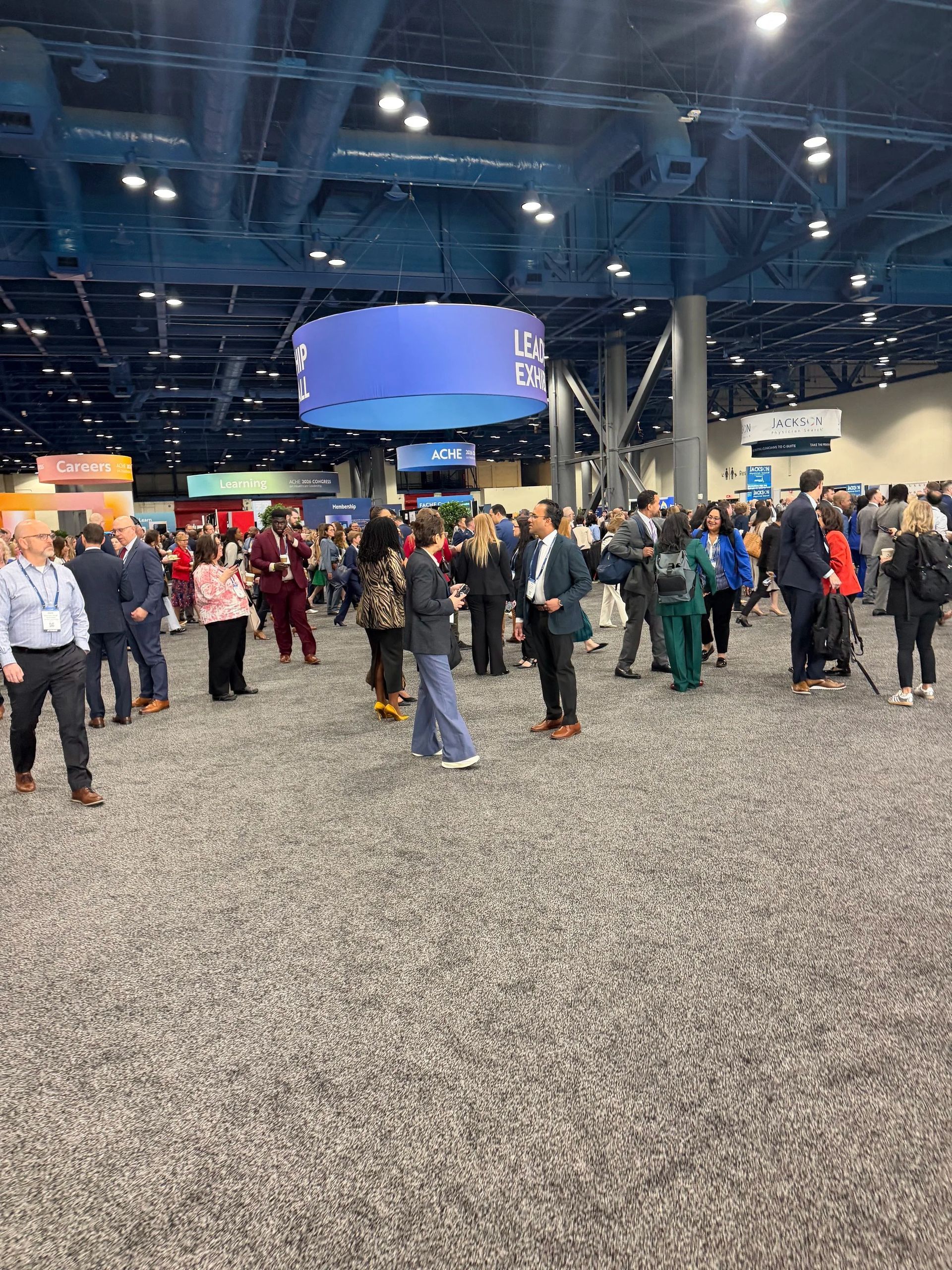 Crowd gathered in a large indoor convention hall with blue ceiling lights and a carpeted floor