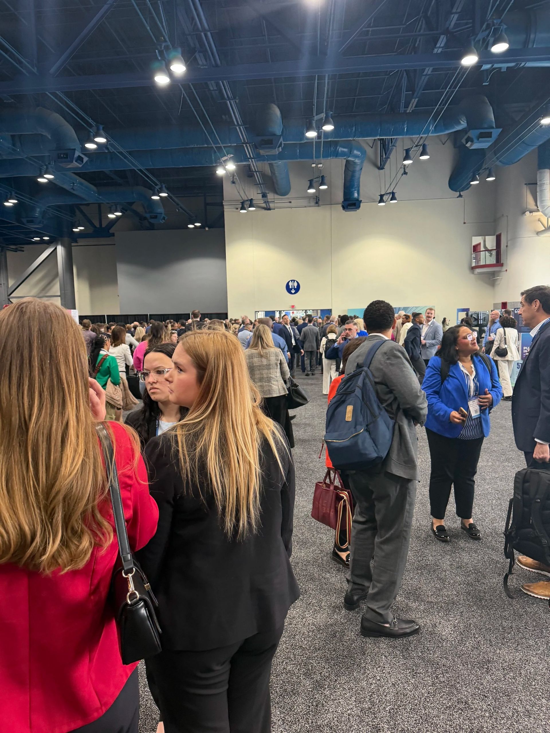 Crowded conference hall with people mingling under blue ceiling lights and hanging banners