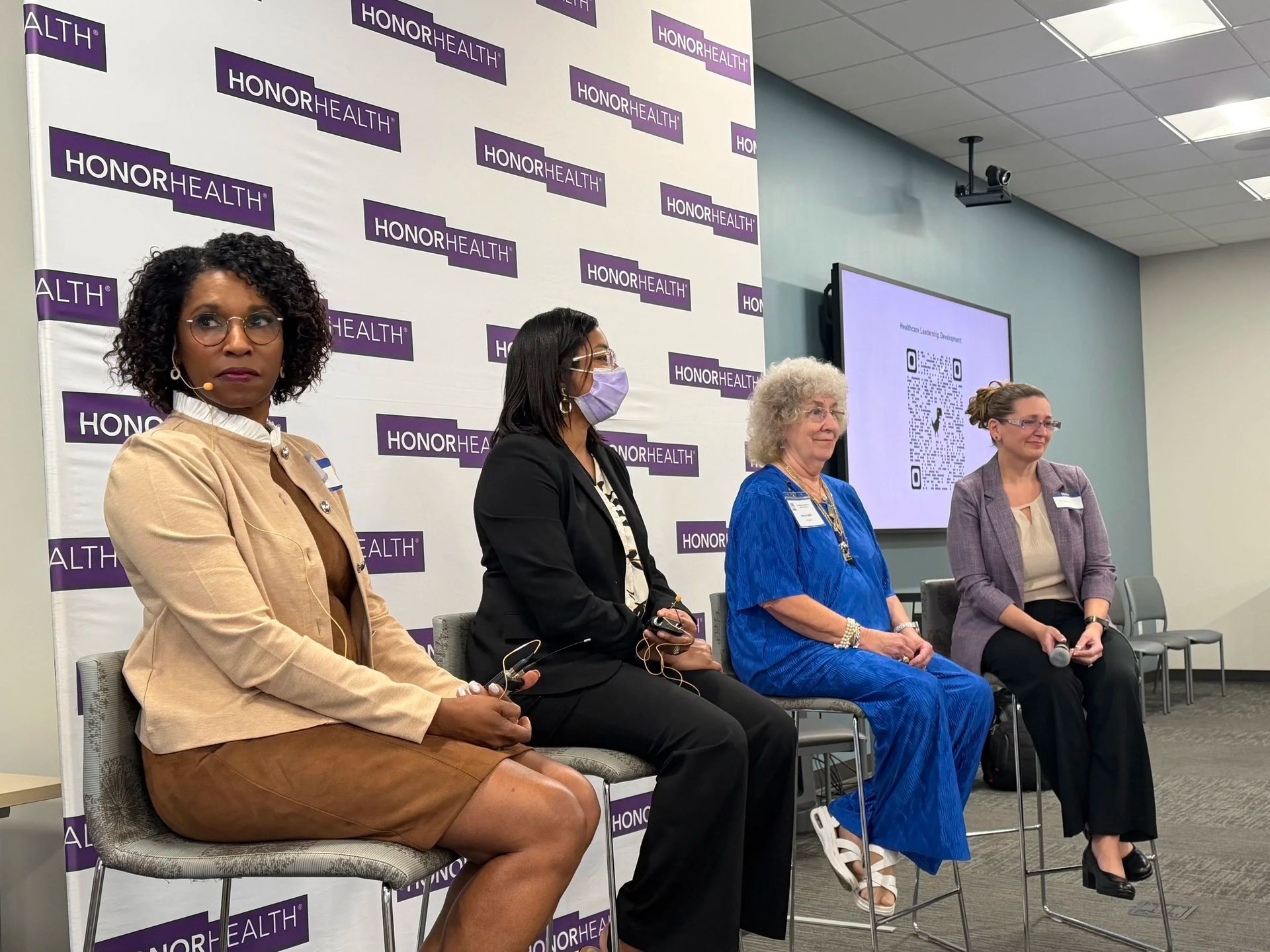 Panel discussion with four seated speakers in a conference room, facing the audience.