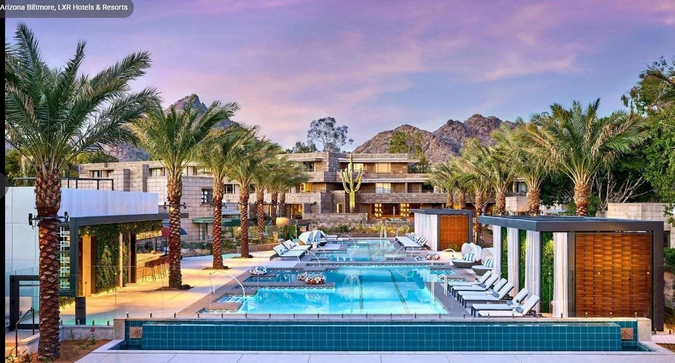 Luxury resort pool with palm trees, loungers, and a waterfront view at sunset