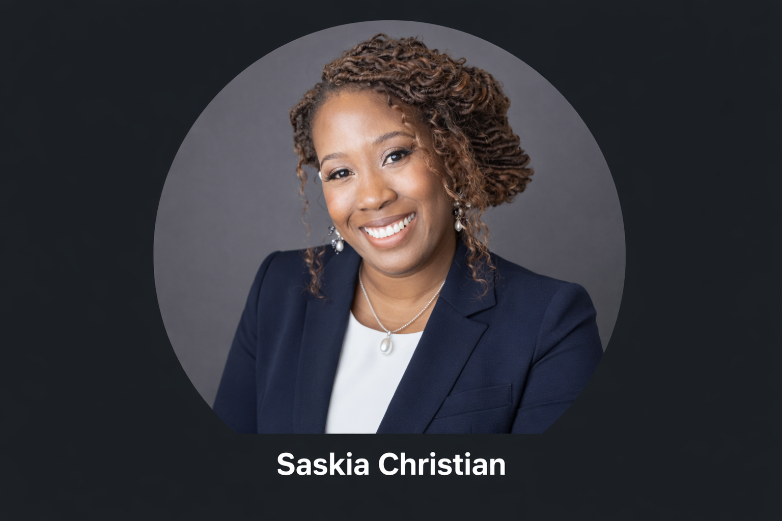 Portrait of Saskia Christian smiling in a navy blazer against a gray background