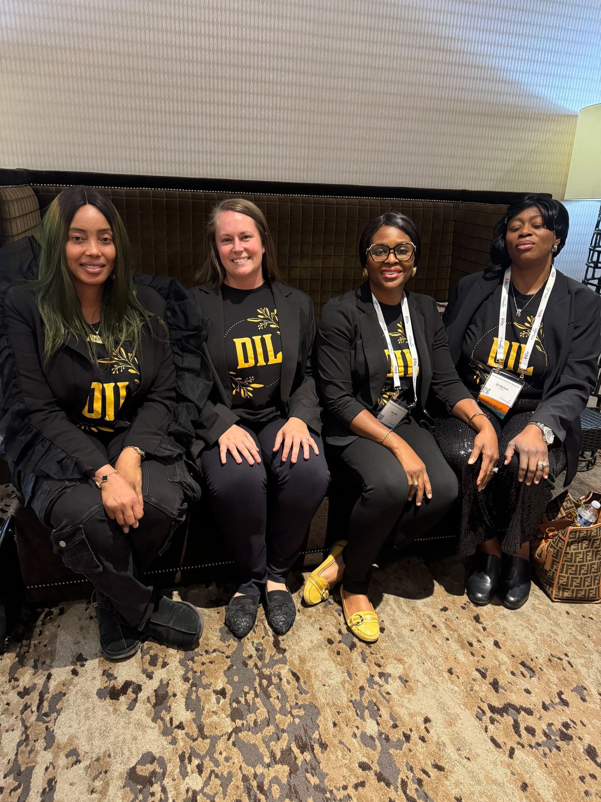 Four people in black and gold matching outfits sit on a couch and smile at the camera.