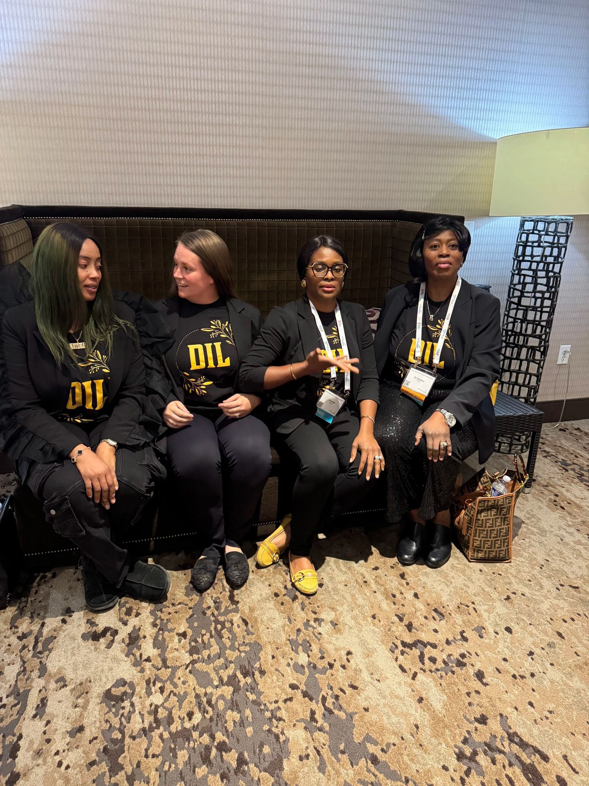 Four people sit on a couch in black outfits with yellow lettering, posing indoors.