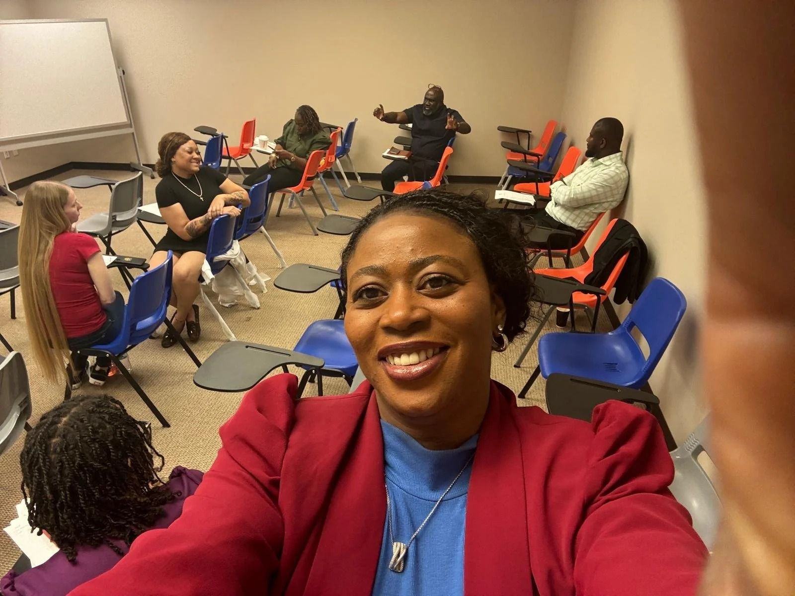 Selfie in a conference room with several people seated on blue chairs around the room.
