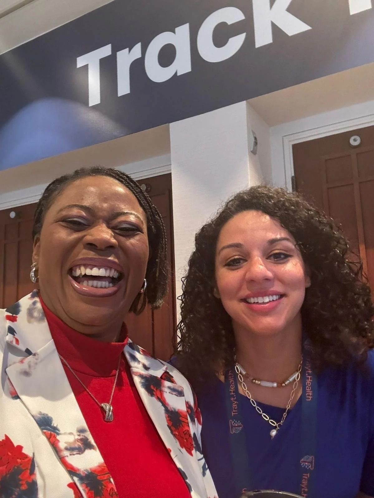 Two smiling women posing indoors under a “Track” sign.