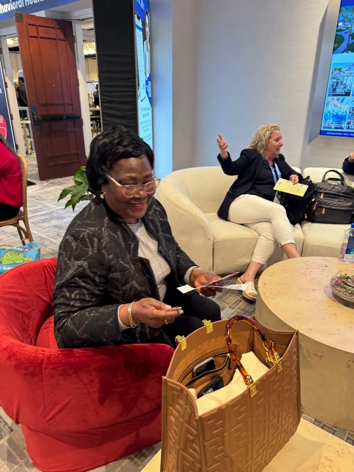 People seated in a hotel lobby, one checking her phone in a red chair.