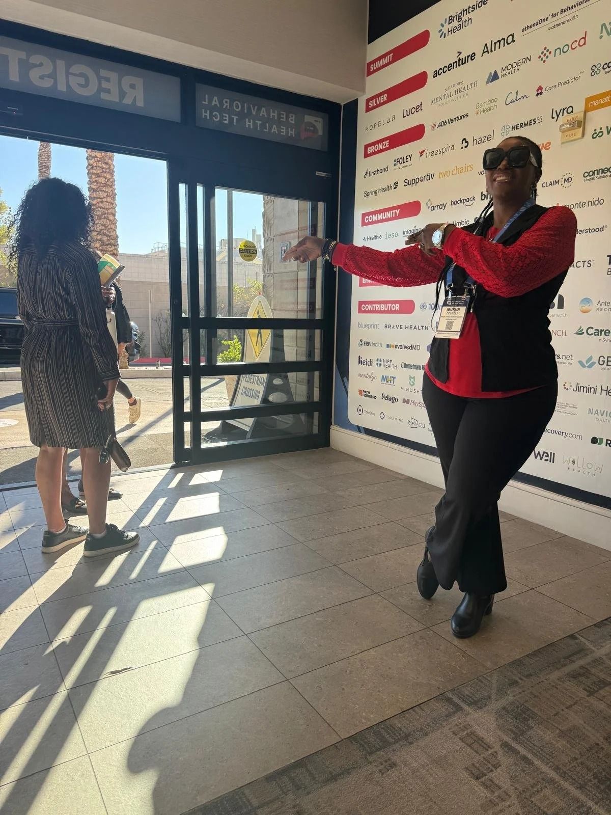 Two people near an entrance; one points while the other stands by the open glass door.