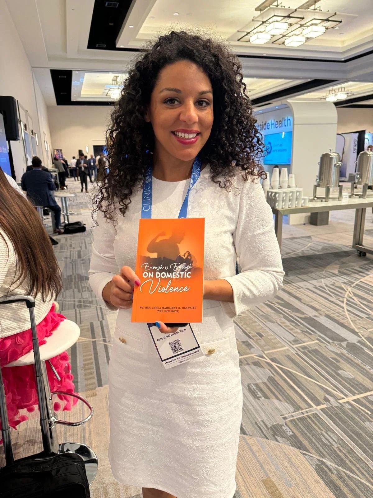 Woman in a white dress holding an orange booklet at a conference hall.