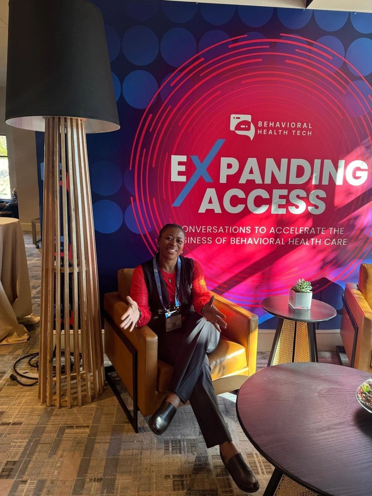 Person seated in a chair beside an “EXPANDING ACCESS” event display with colorful circular graphics