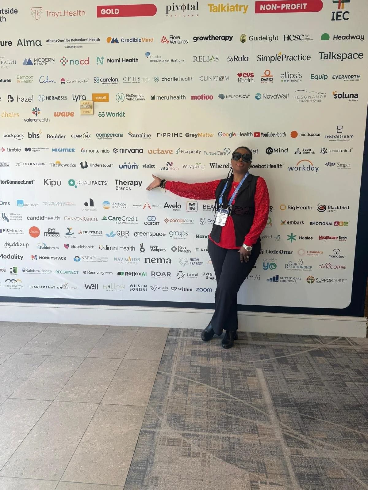 Person in red jacket pointing at a logo-covered wall in a lobby.