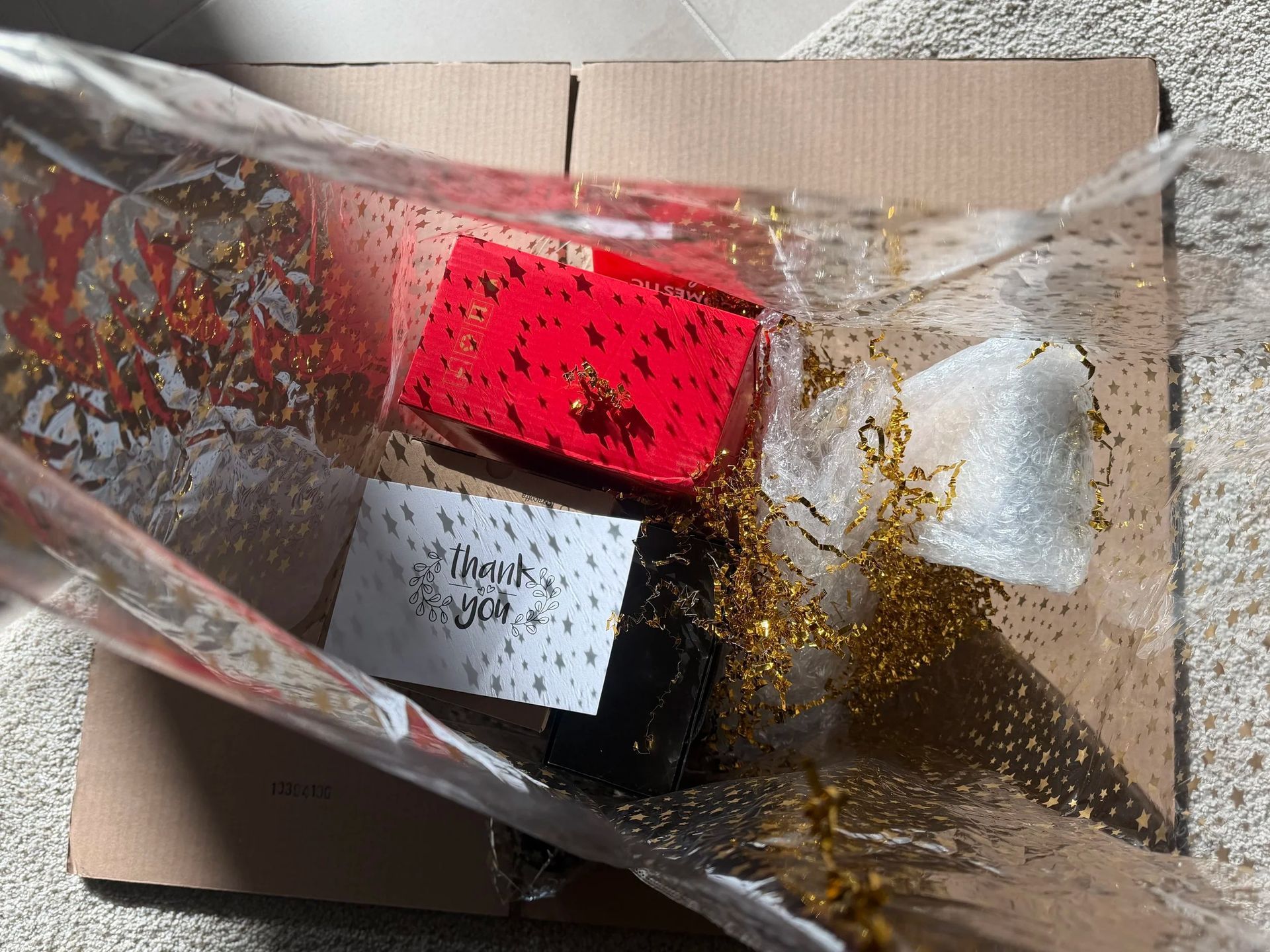 Open cardboard box with crinkled clear plastic and red, white, and black packaged items inside.