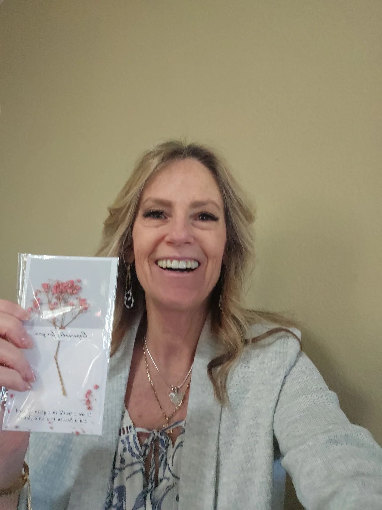 Woman smiling and holding up a floral greeting card against a beige wall.