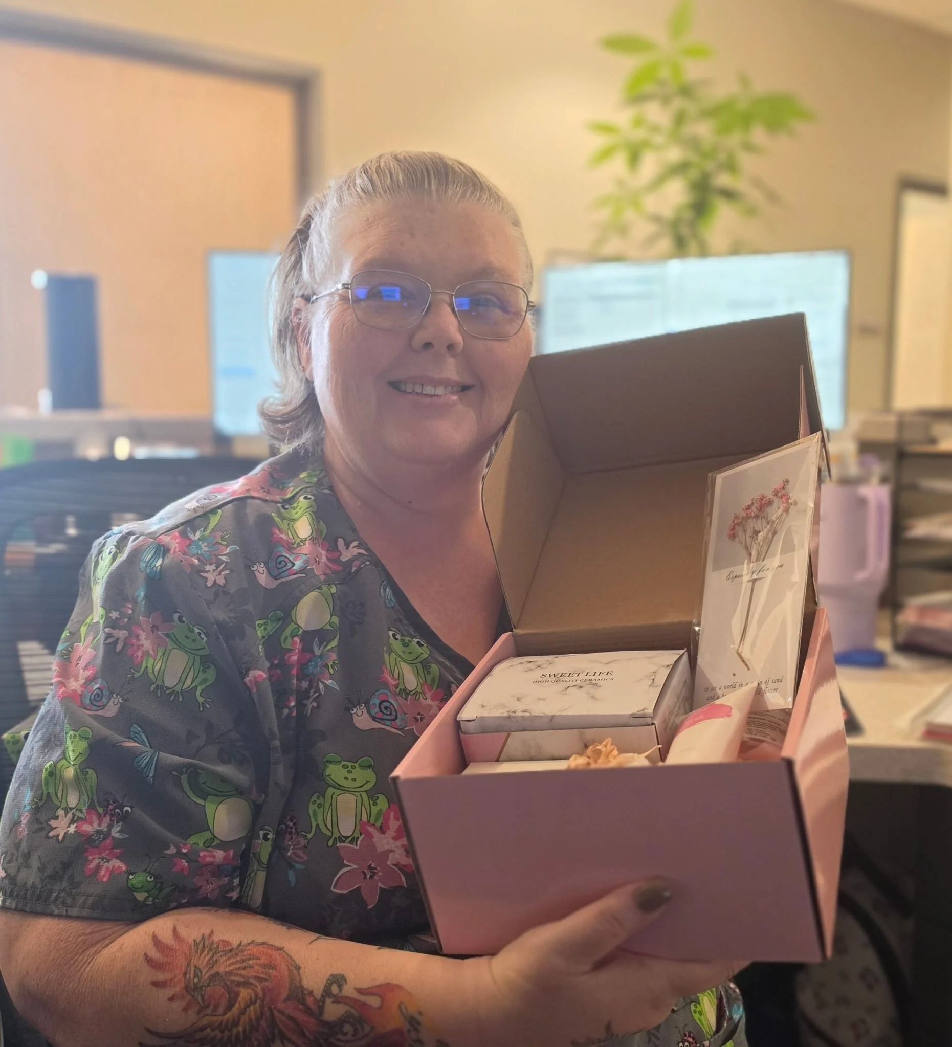 Smiling person holding an open pink gift box in an office setting