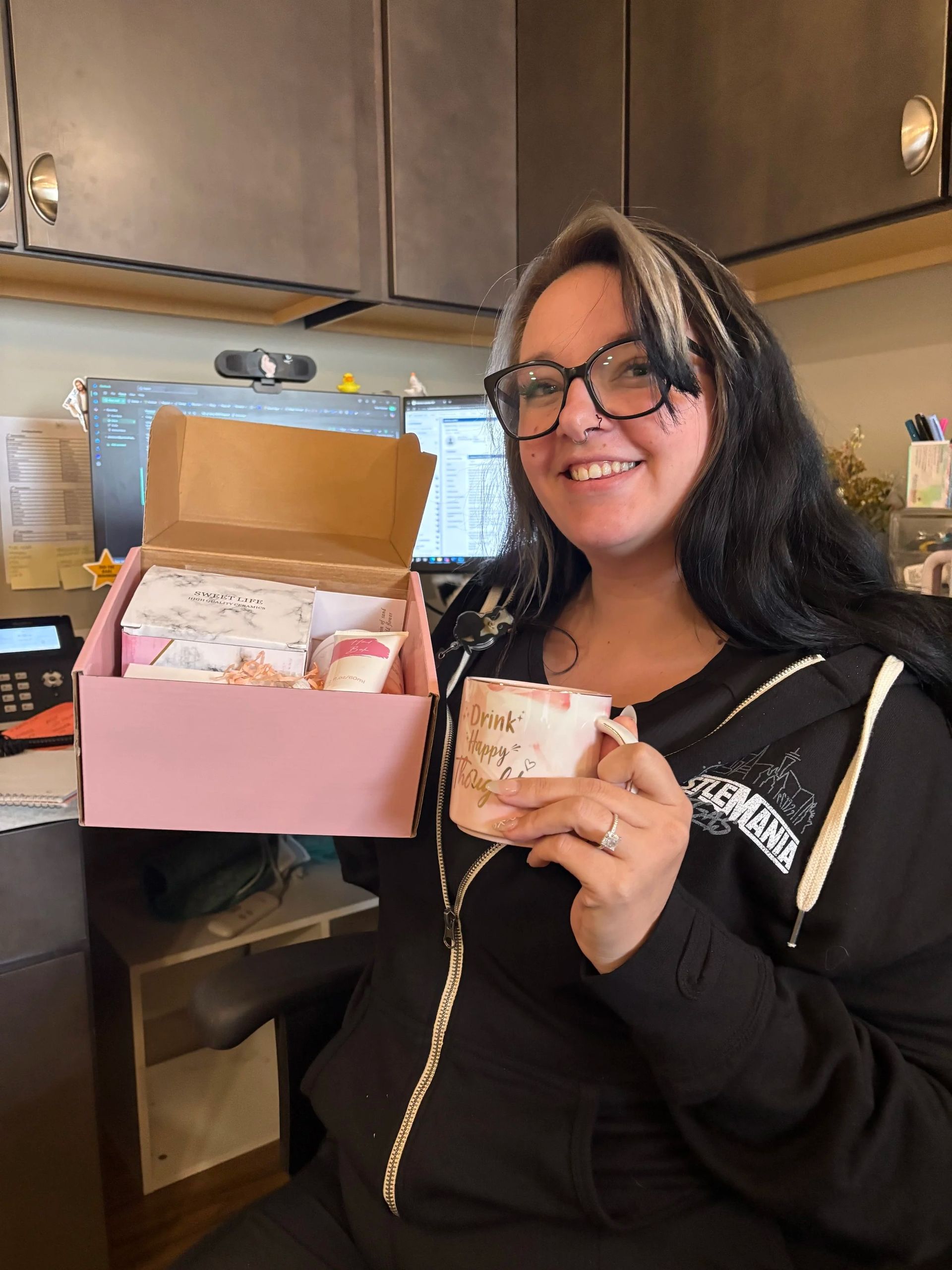 Woman smiling in a kitchen, holding an open pink gift box and a matching cup.