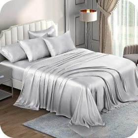 White bedding on a neatly made bed in a softly lit, modern bedroom with gray accents and sheer curtains