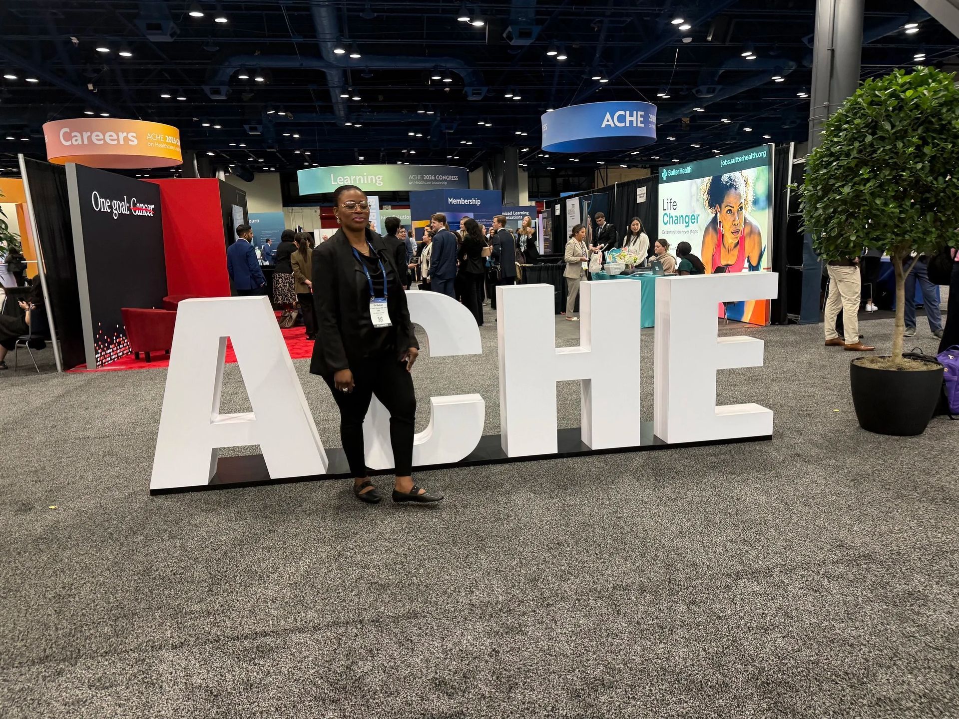 Large white AHE letters at a trade show, with a person standing in front of them.