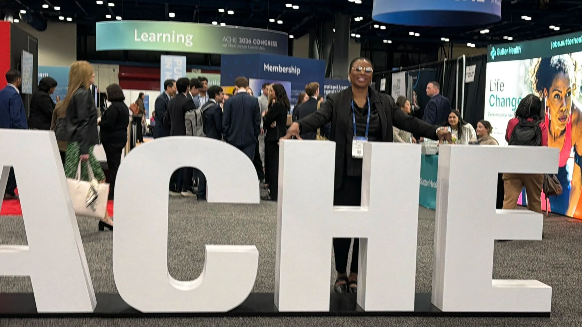 Large white “CACHE” letters at a trade show booth with people standing behind them