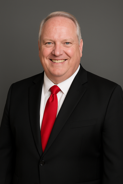 Smiling man in a black suit with a red tie against a gray studio background