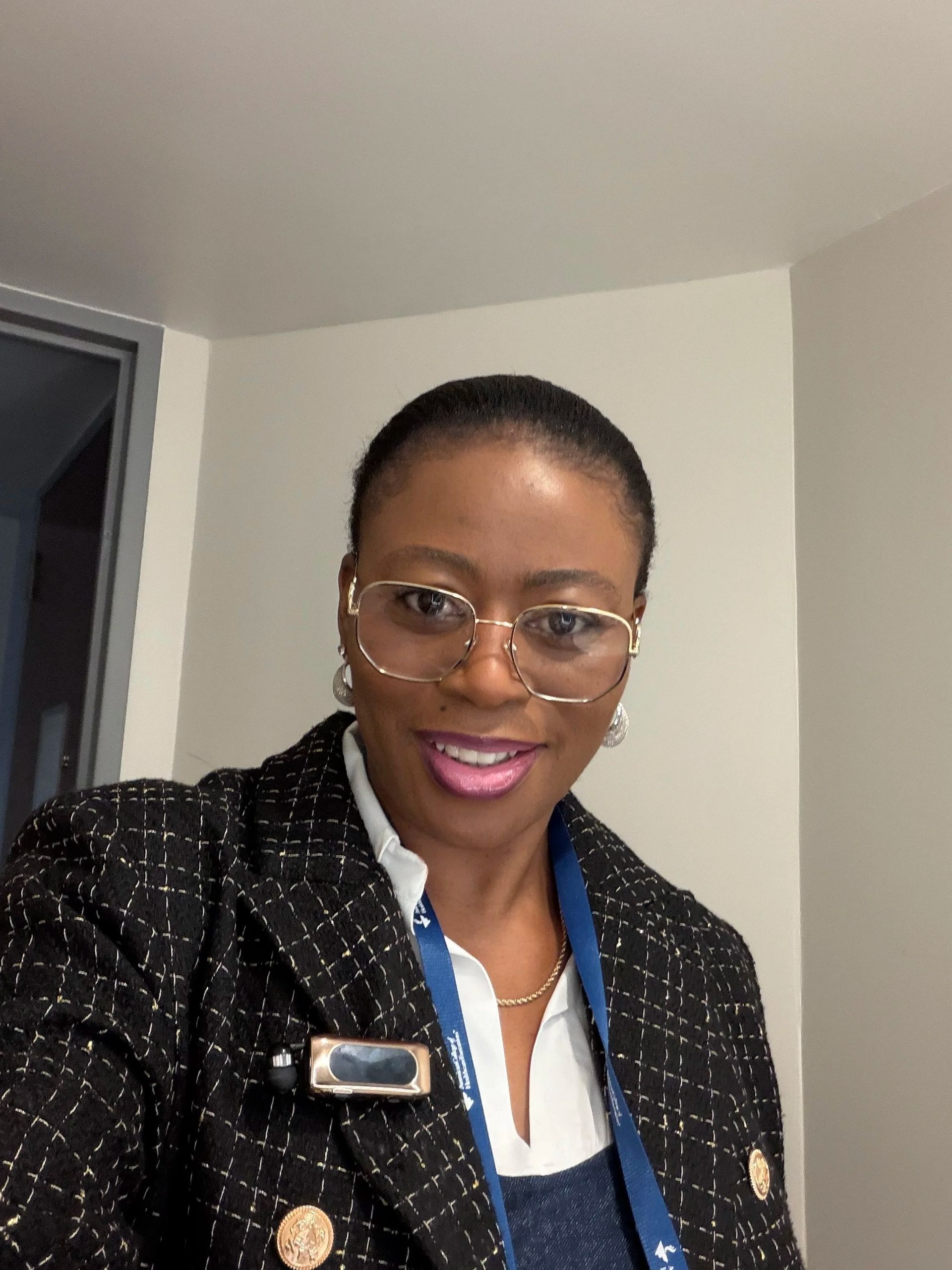 Smiling person wearing glasses and a black blazer in a room with white walls