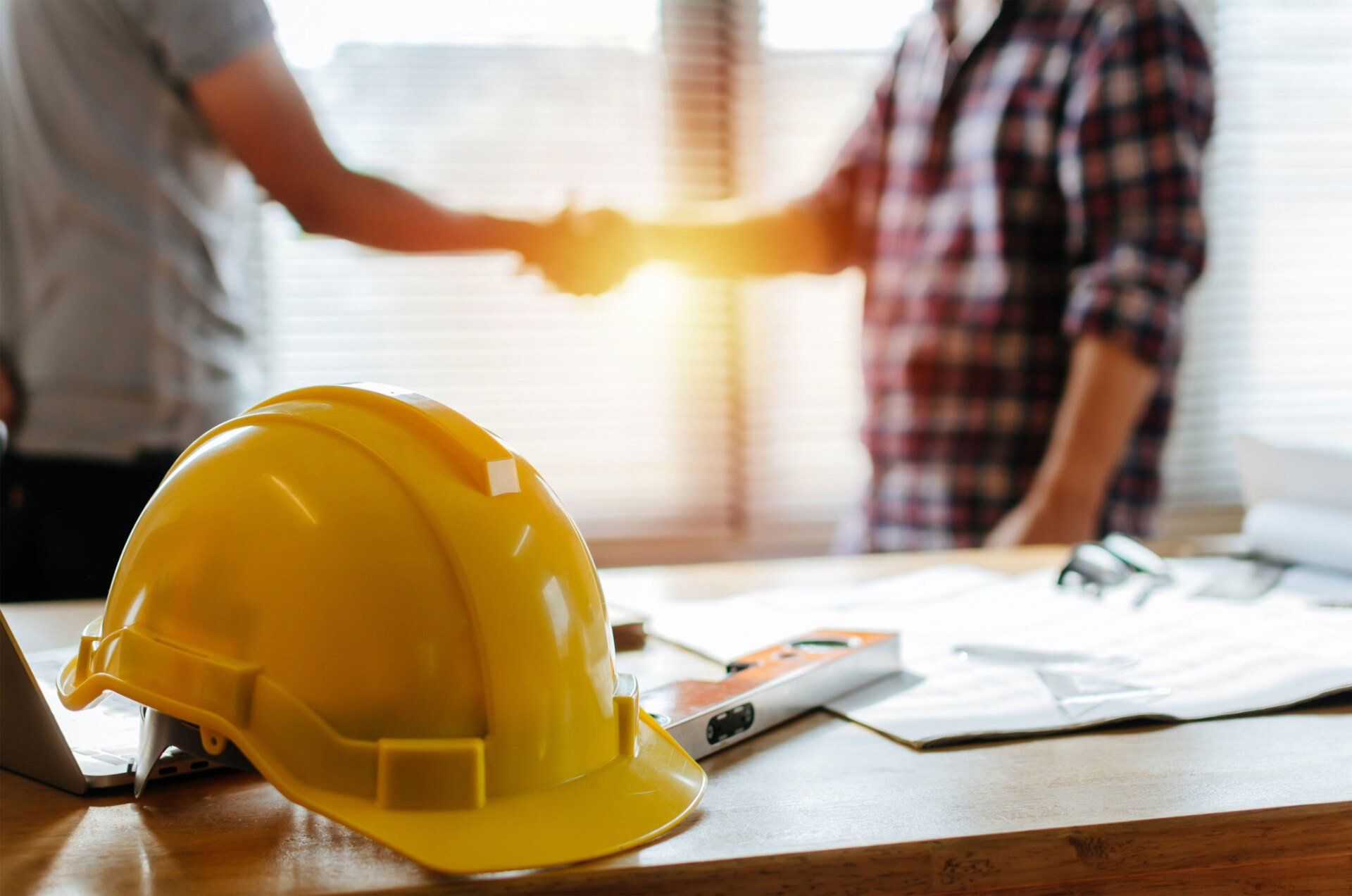 Yellow hard hat on a construction table with two workers shaking hands in the background