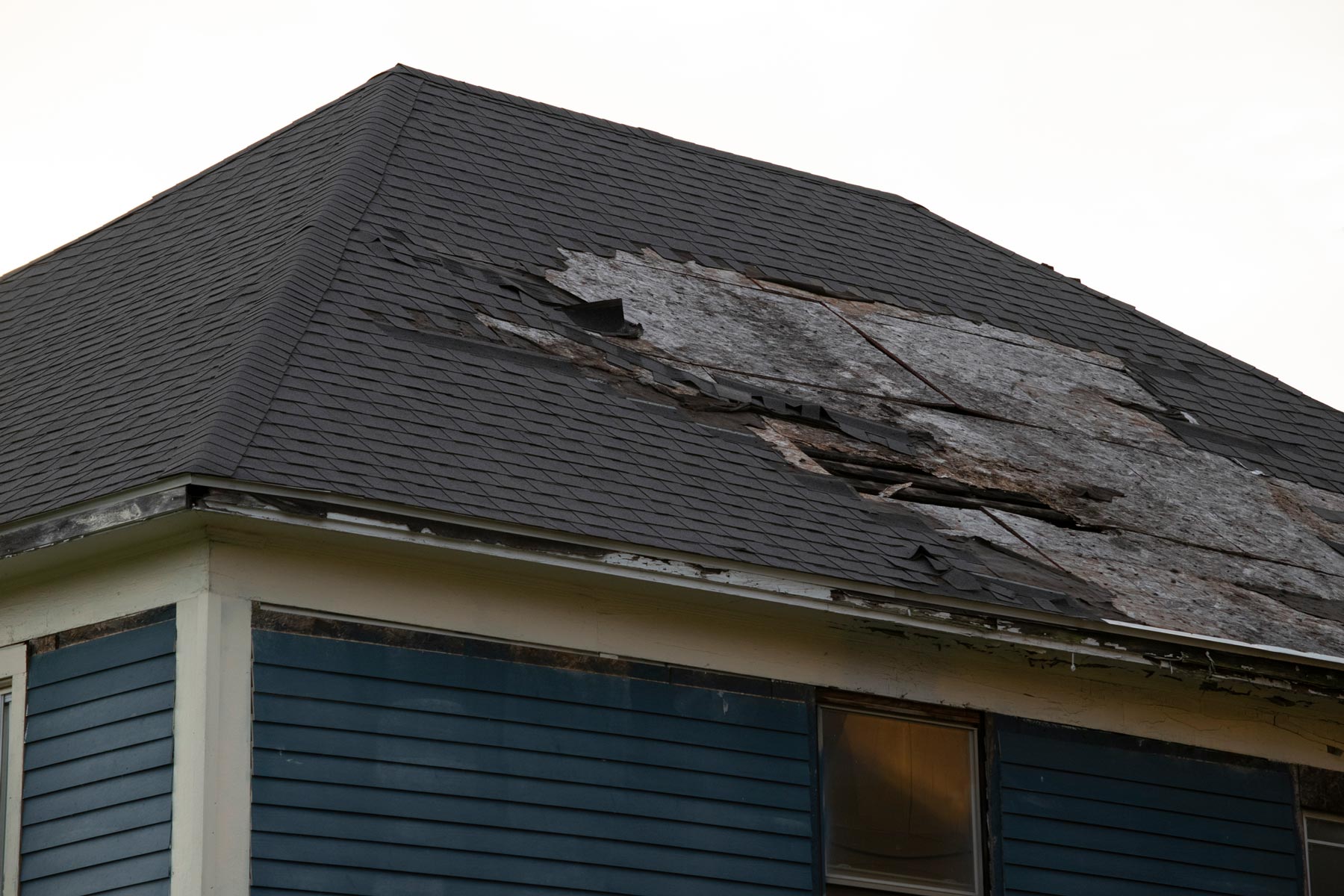 Damaged roof with a large stripped, dark patch on a house exterior