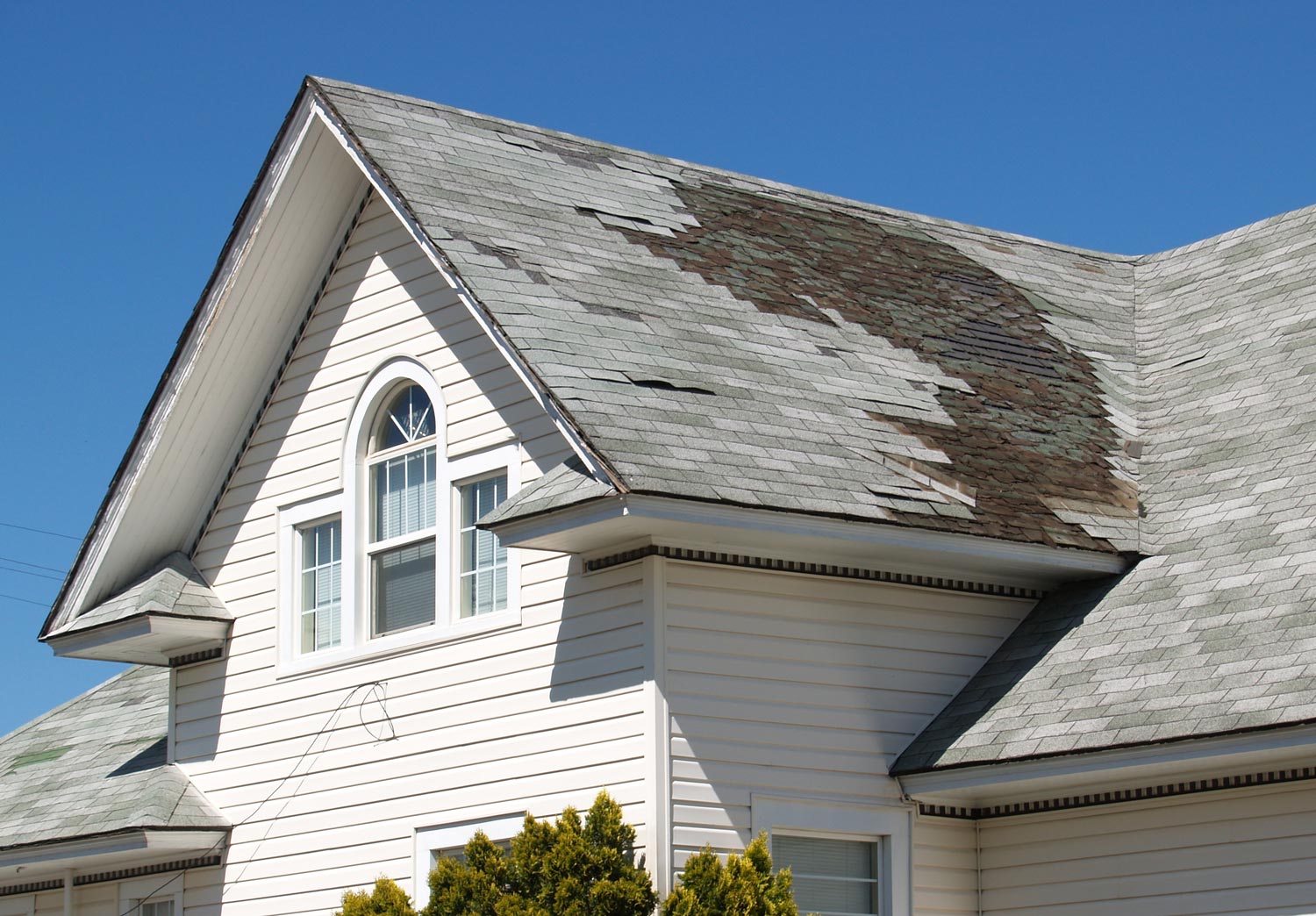 White house roof with dark weather stains and damaged shingles under a blue sky