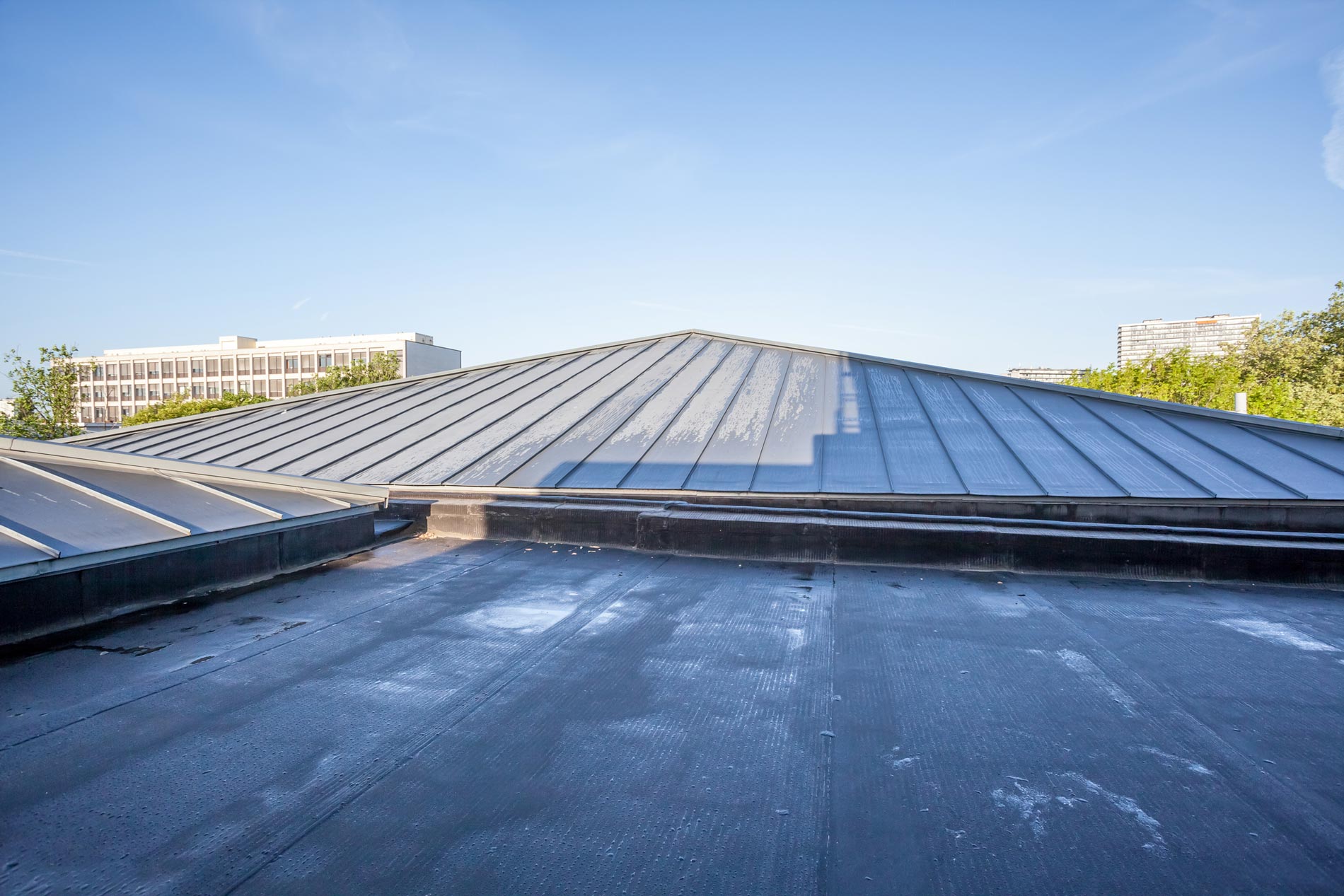 Solar rooftop with dark panels under a clear blue sky, viewed from a low angle.