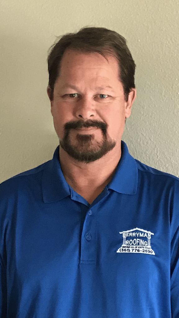 Man in blue polo shirt standing against a beige wall, facing the camera.
