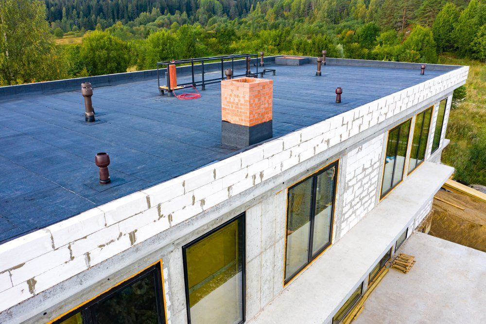 Flat-roofed white building with black rooftop membrane, skylights, and forested background