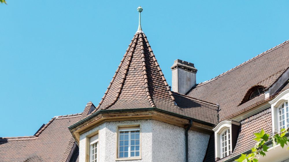 Historic house roof with a steep conical turret, white walls, and blue sky背景