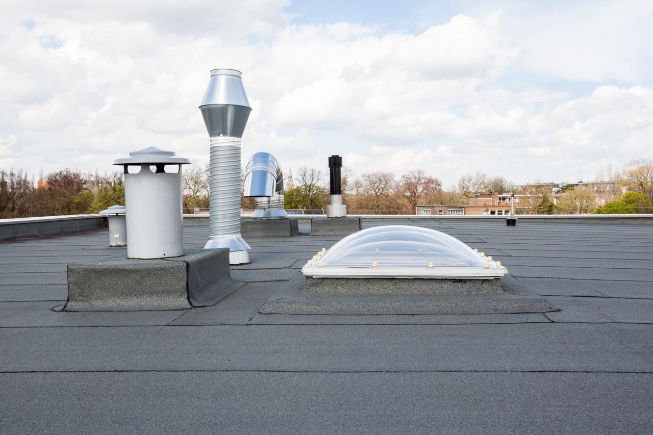 Rooftop with several vent pipes and a white skylight under a cloudy sky.