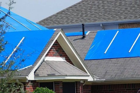 House roof covered with blue tarps after storm damage