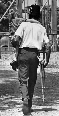 Person walking away on a dirt path, holding a camera, with a dog perched on their left shoulder.