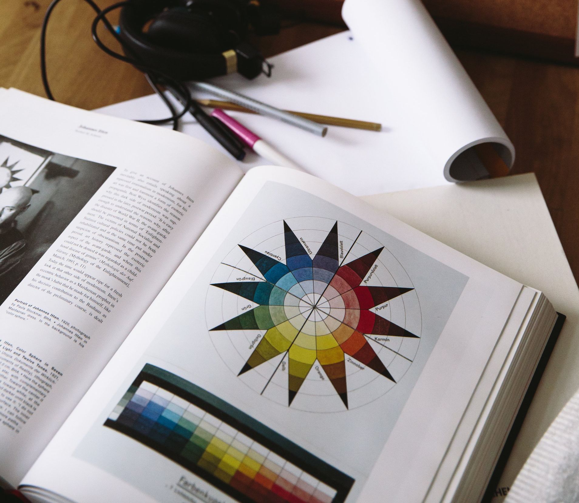 Open book with a color wheel diagram and color palette examples, with pens, pencils, and paper nearby.