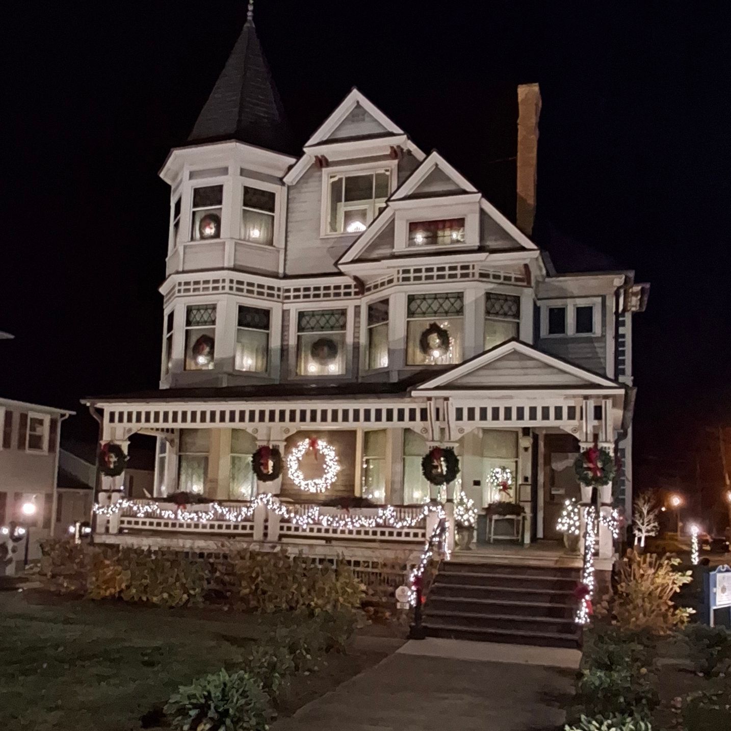 Victorian house lit up for Christmas with wreaths, garlands, and lights at night.