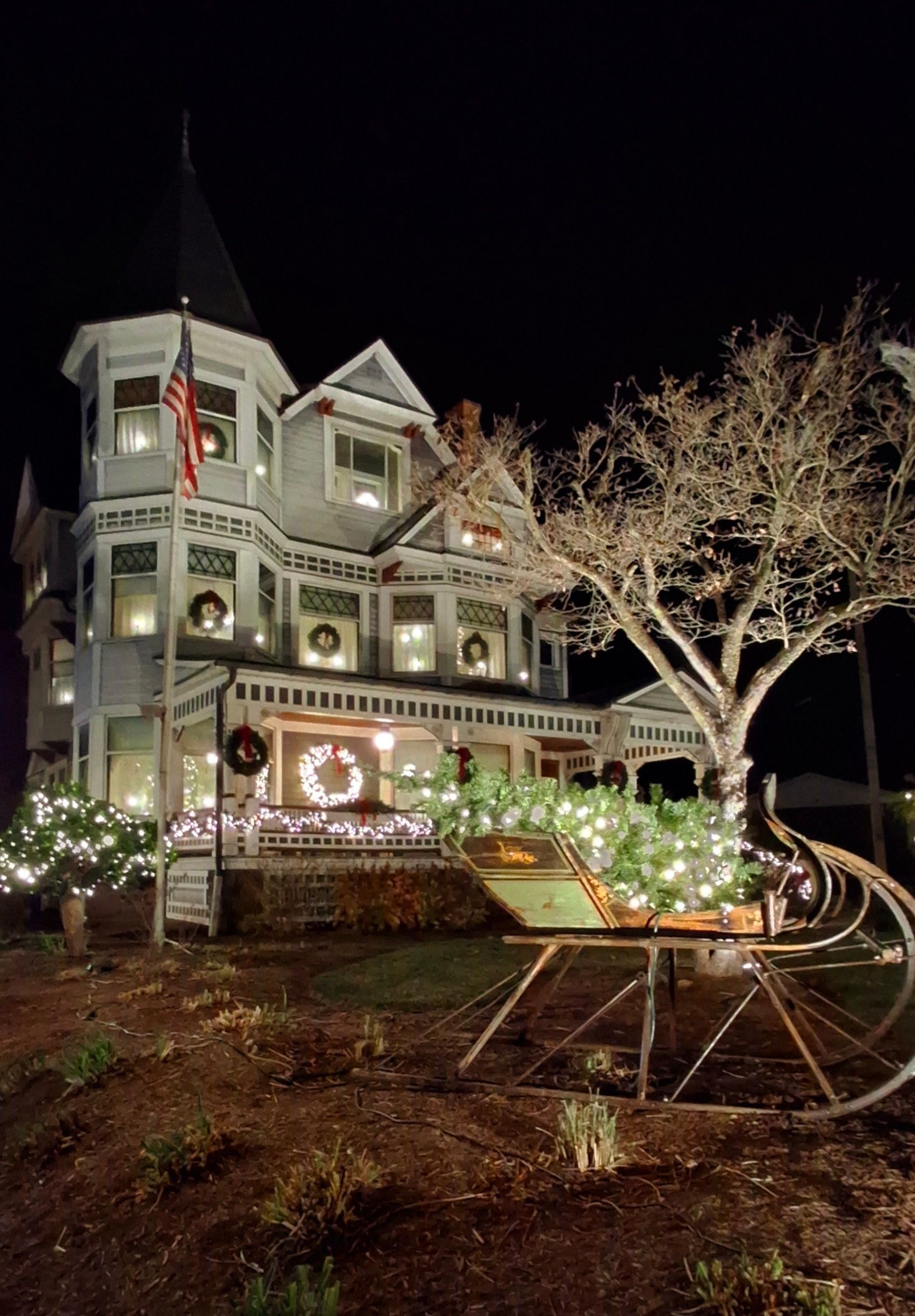 Festive Victorian house at night, decorated with Christmas lights and wreaths; a sleigh is in the foreground.