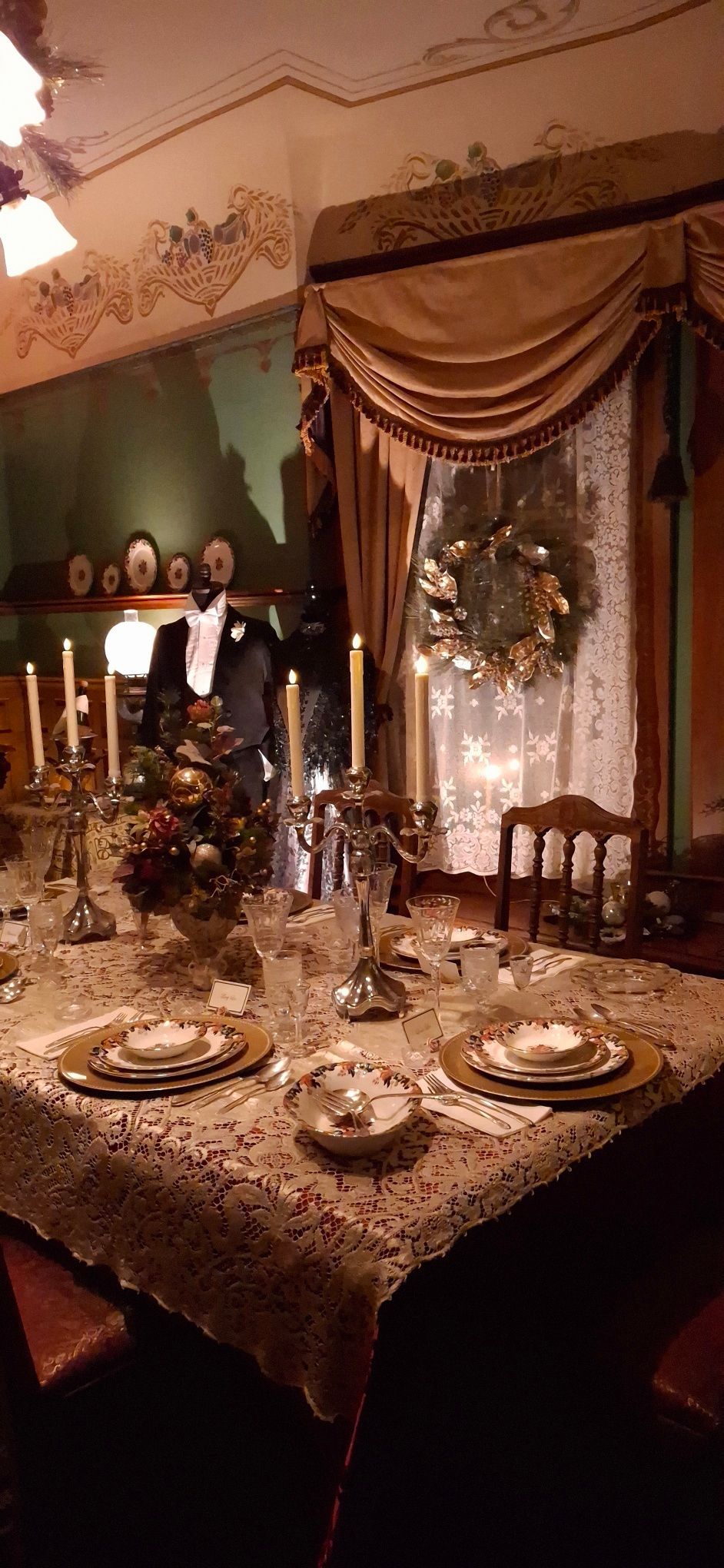 A Christmas dinner table set in a vintage room with candles, a wreath, and elegant decorations.