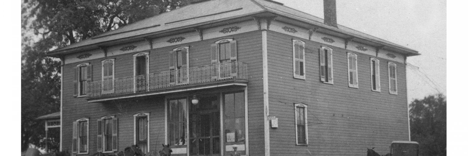 Black and white photograph of a two-story building with a front porch and second-story balcony.