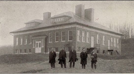 A two-story brick building with five men standing in front.