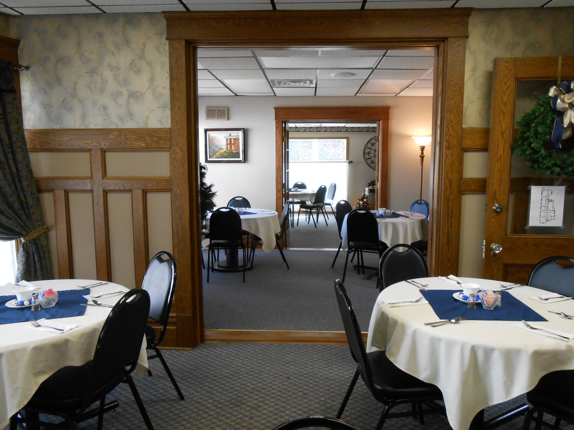 Restaurant dining room with round tables set for a meal. Another room visible through doorways, also set with tables.