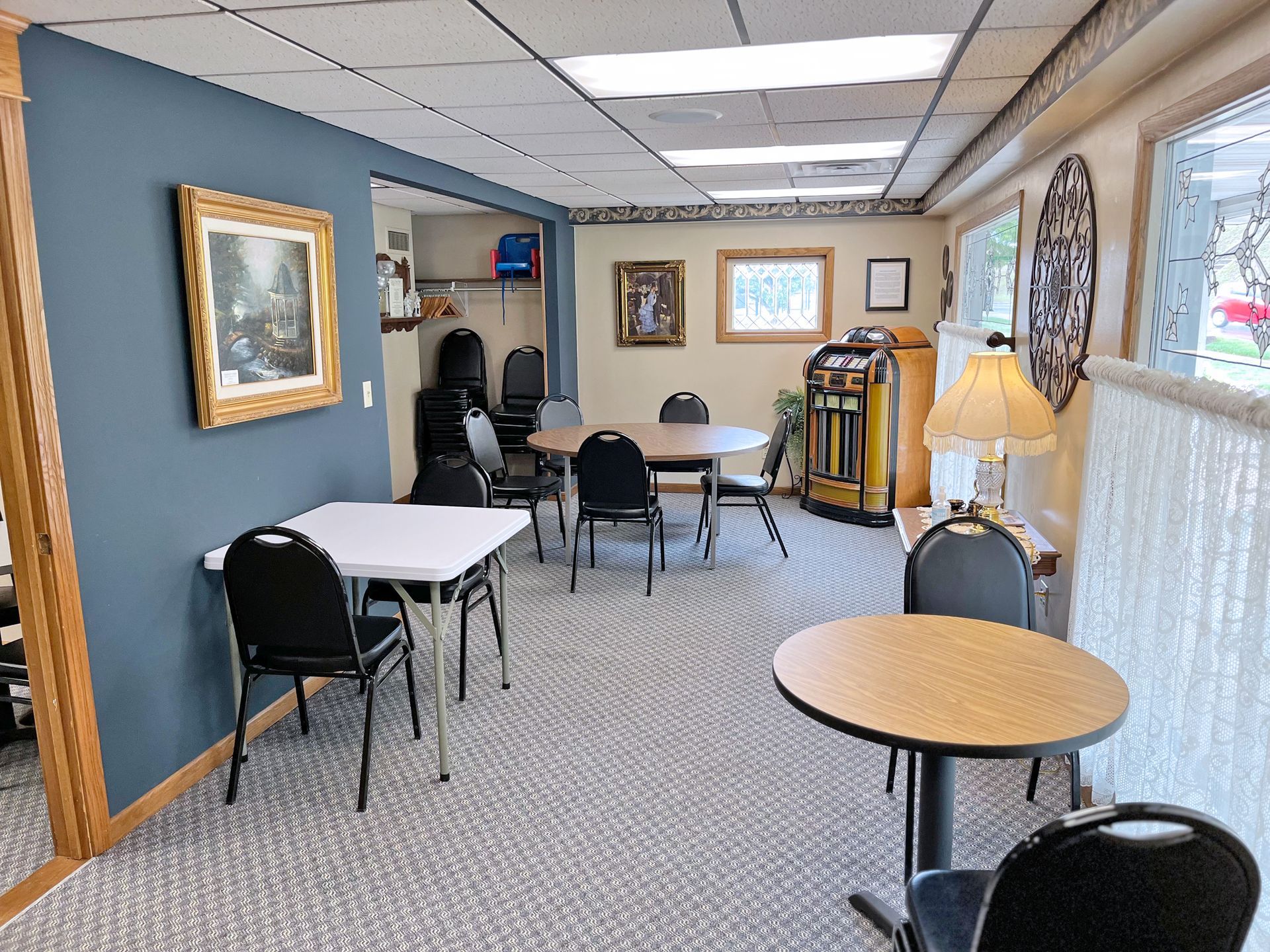 A community room with tables and chairs, art on walls, and a vintage jukebox.