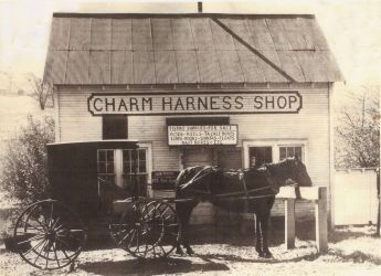 Charm Harness Shop, horse-drawn buggy parked outside small wooden building. Sign reads shop name, with additional text below.