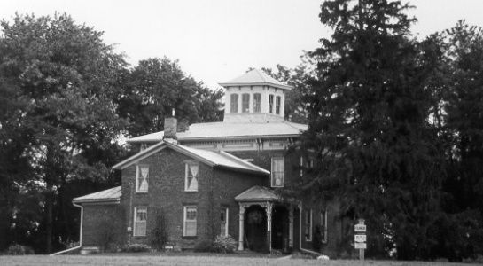 Brick house with a rounded cupola roof, surrounded by trees, on a cloudy day.