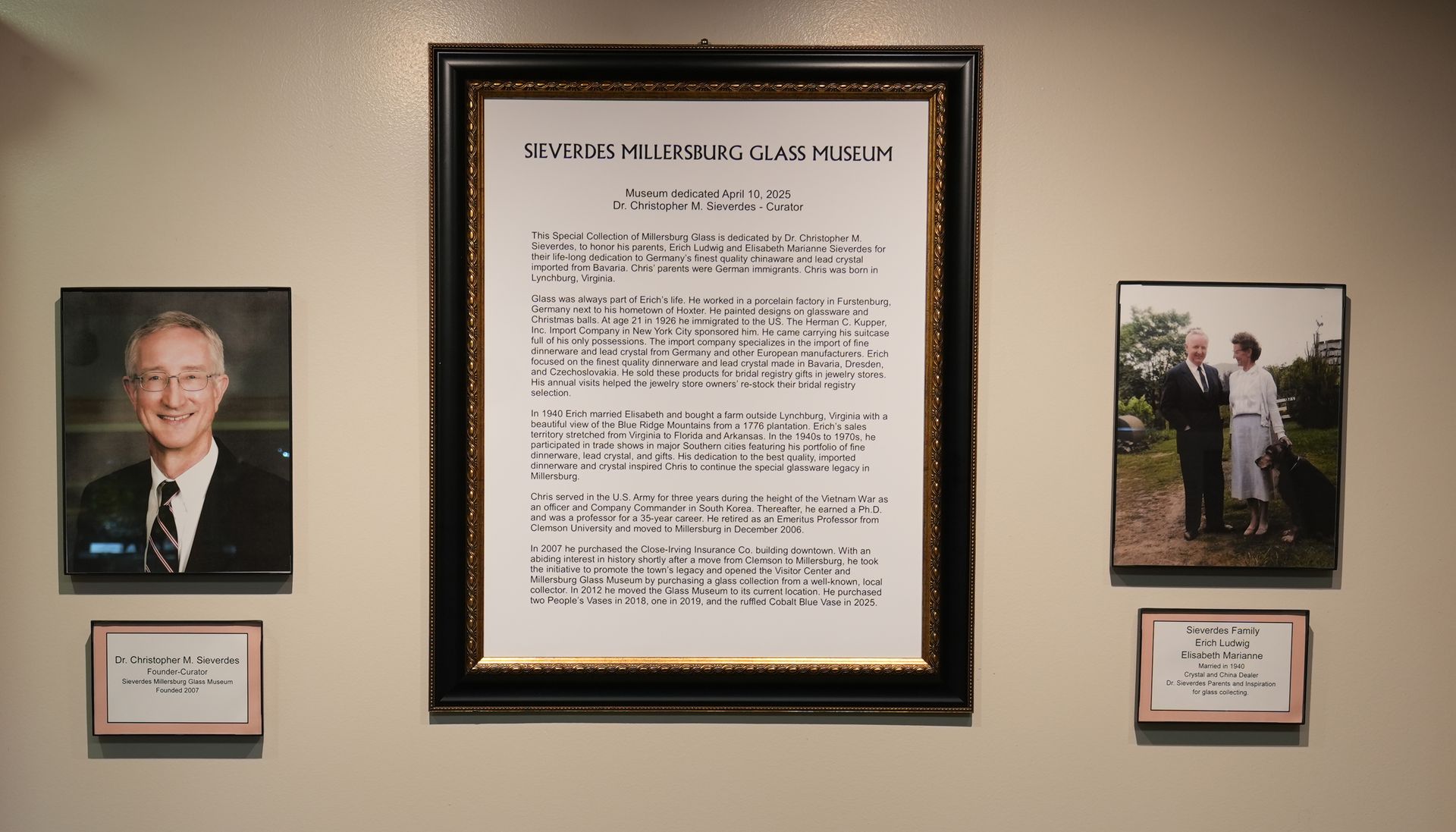 Wall display with a framed document and photos; a portrait, and a photo of two people.