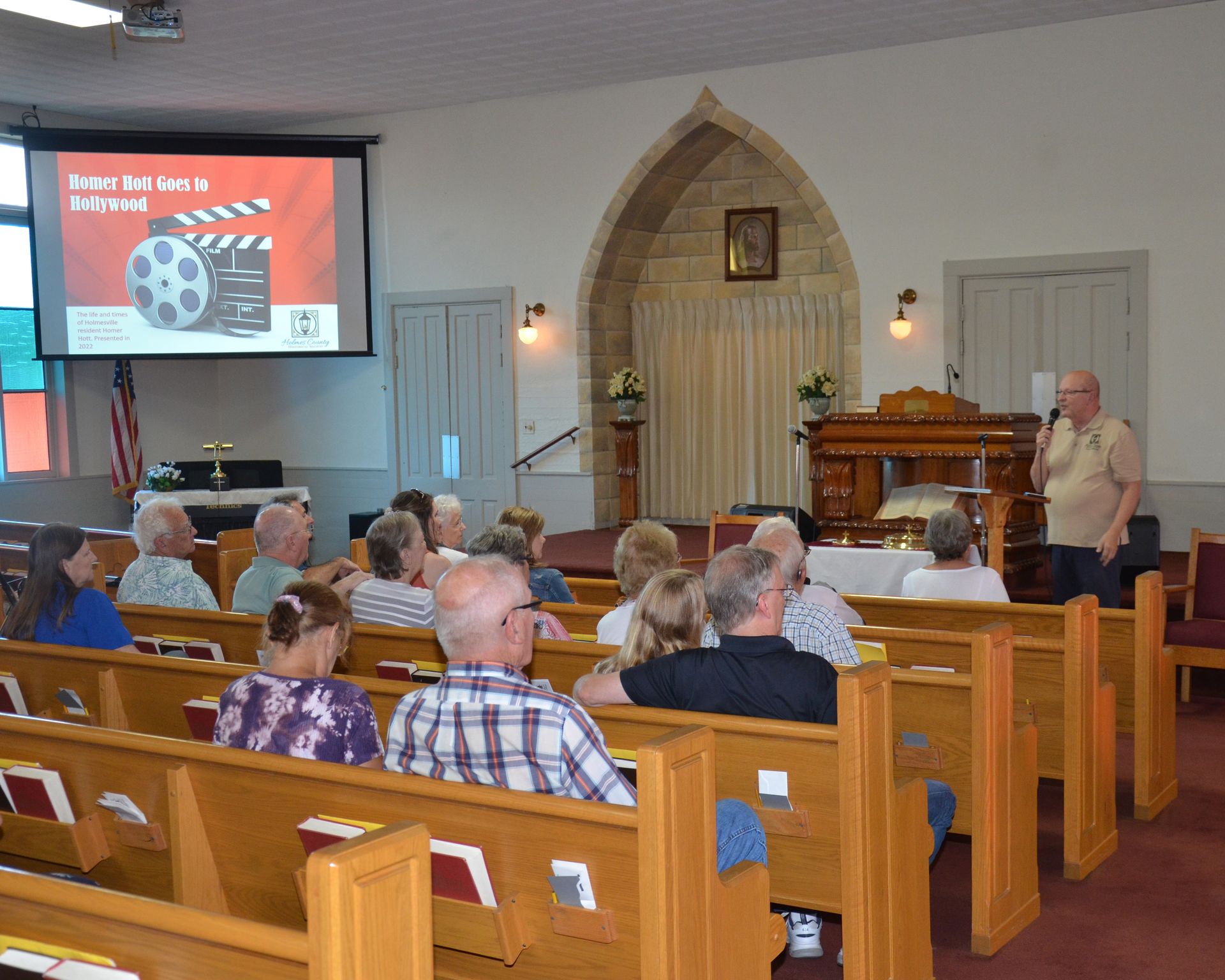 People seated in a church watching a presentation, with a speaker at the front.